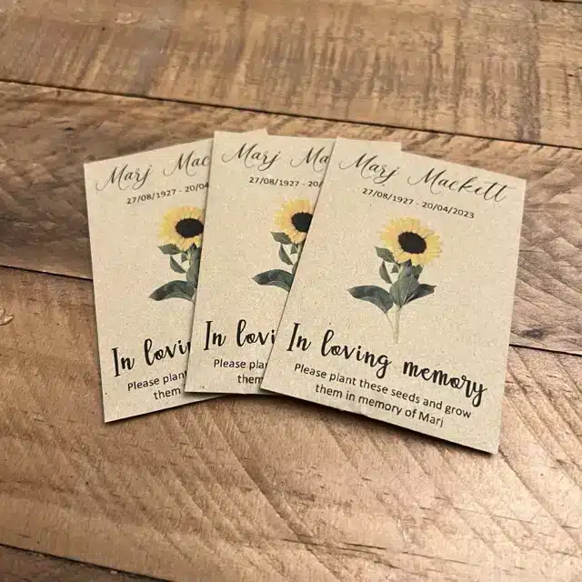 Three personalised funeral seed brown envelopes featuring a sunflower design ready for guests at a memorial service.